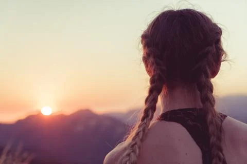 Girl faces sun setting behind mountains Stock Photos