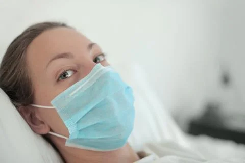 Girl feeling sick, lying in the bed wearing a face mask Stock Photos