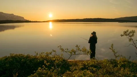 A girl fishing in front of a beautiful midnight sun. Stock Photos