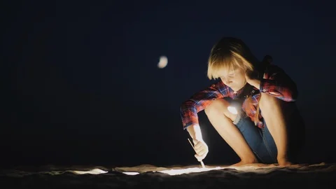 A girl with a flashlight in her hand is looking for something on the beach in Stock Footage 93866974
