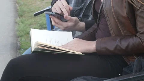 Girl flipping through the book while the boy is using the phone 스톡 동영상 90182542