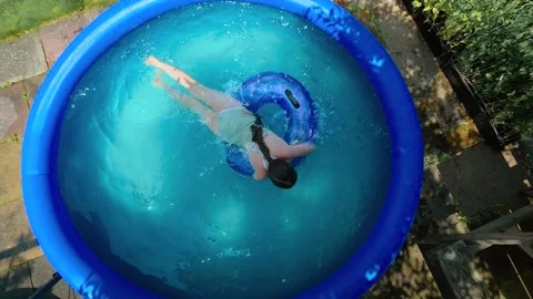 Girl floating on swim ring in backyard inflatable pool during extreme summer Stock Footage 340553969