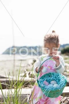 Girl Gathering Easter Eggs In Basket On Beach