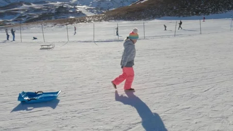 Girl getting ready to slide down snowy slope on blue sled Stock Footage 306680422