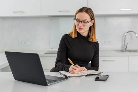A girl with glasses makes notes in a notebook, working for a laptop at home 写真素材
