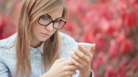 Girl with glasses is typing a message on the phone on a red background Stock Footage 55491663