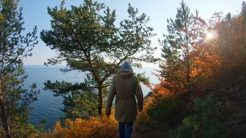 Girl goes down a path on steep slope of sea shore on bright sunny autumn day Stock Footage 123973788