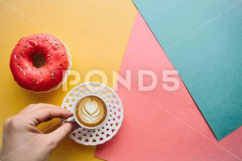 The girl is going to drink coffee and eat donut which lie on the colored surface Stock Photos