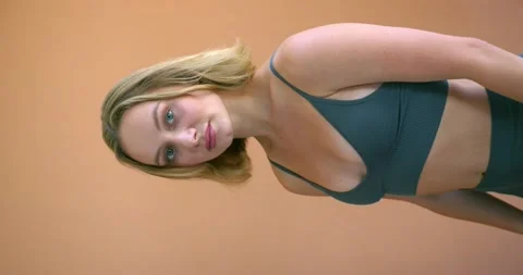 Girl in a gray top on brick-colored background looks camera and fixes her hair Video stock 204091653