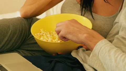 Girl with a guy eating popcorn while watching a video on a laptop Stock Footage 166510625