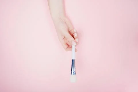 Girl hand hold white brushes makeup on pink color background. Top view flat lay Stock Photos