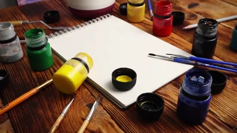 Girl hand puts different bruches on a painting surface Notebook gouache colo Stock Footage 295125949
