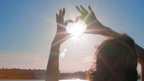 The girl from the hands made a heart shape at sunset, on the sea, against an Stock Footage 101914385