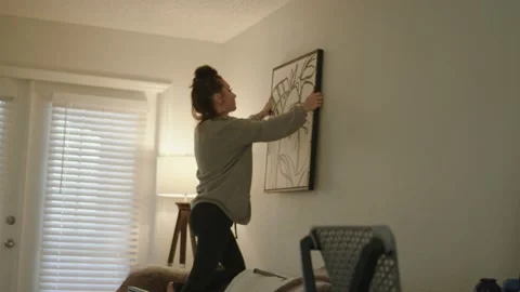 Girl hanging up canvas on apartment wall Stock Footage