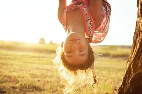 The girl is hanging upside down on a tree in summer in orange sunlight and a  Stockfoto's