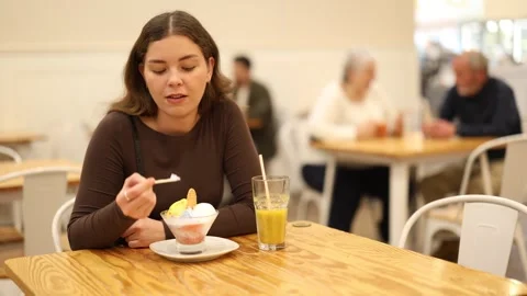 Girl happily eats delicious ice cream while sitting at a table in a cafe Stock Footage 343715167