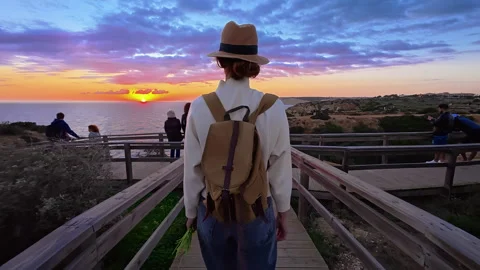A girl in a hat and with a backpack goes to the edge of a cliff on Ponta de Stock Footage 314660947