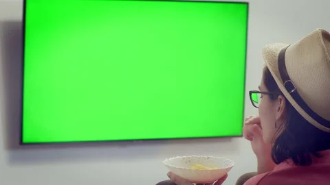 Girl in the hat eats popcorn out of a bowl and watches TV, chroma key Stock Footage 195013951