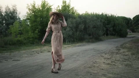 The girl in the hat goes and turns around against the background of trees. Slow 스톡 동영상 154976053
