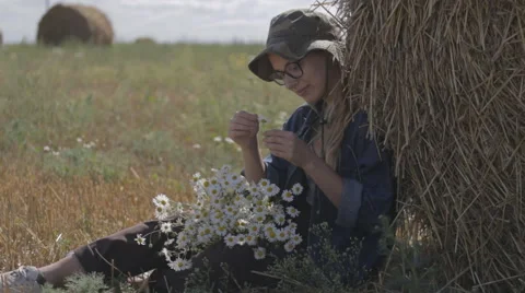 Girl in the hat guesses on camomile at the stack of straw Stock Footage 67374426