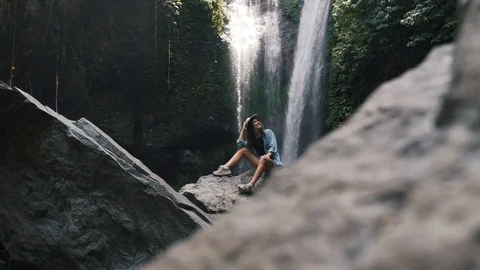 Girl in a hat is resting on the background of a waterfall Stock Footage 129057091