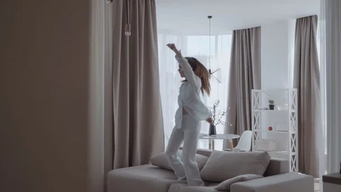 Girl having fun and jumping on sofa In the interior of the apartments Stock Footage 129814433