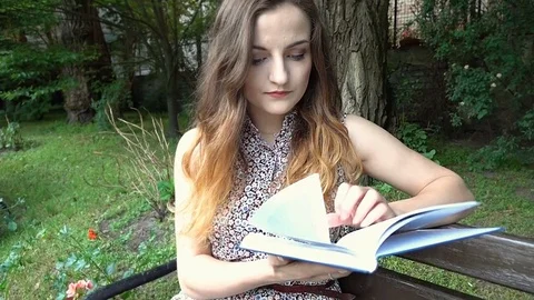 Girl having painful headache while reading book in the park, steadycam shot Stock Footage