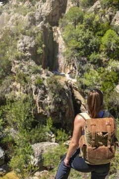 Girl on her back with backpack looking at a waterfall from the top of a canyo Stock Photos