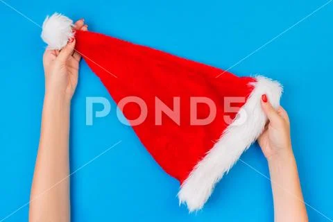 Girl hold in hand Santa Claus red hat on blue background, top view Stock Photos