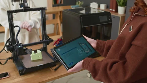 Girl Holding Tablet with Instructions While Working on 3D Printer with Classmate Stockbeeldmateriaal 335692822