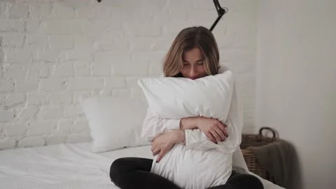 Girl hugging a pillow while sitting on the bed Stock Footage 168749991