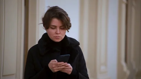 A girl in a jacket with a large collar is typing a message on her phone Stock Footage 114229809