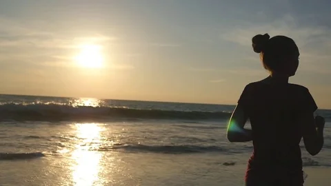 Girl jogging along ocean shore during sunrise. Silhouette of young woman running Stock Footage
