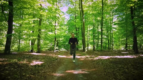Girl jogging through a sunlit forest trail, surrounded by lush green trees .. Stock Footage 307828178