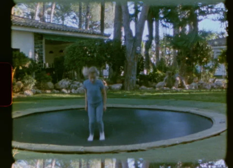 Girl jumping on trampoline view from backyard 8mm Stock Footage 332406599