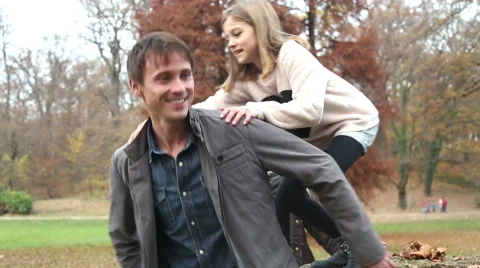 Girl jumps on dad's back in the park Stock Footage 59553983