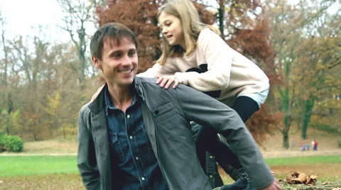 Girl jumps on dad's back in the park Stock Footage 59553986