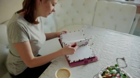 The girl in the kitchen sits on the couch at the table, leafs through a notebook Stock Footage 150437396