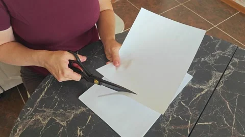 A girl at the kitchen table cuts white paper with scissors Stock Footage 316789419