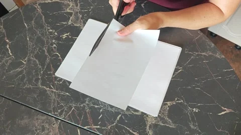 A girl at the kitchen table cuts white paper with scissors Stock Footage 316789567