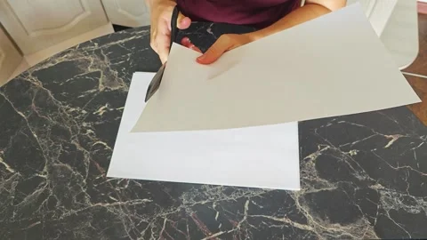 A girl at the kitchen table cuts white paper with scissors Stock Footage 316789570