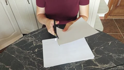 A girl at the kitchen table cuts white paper with scissors Stock Footage 316789779