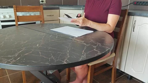 A girl at the kitchen table cuts white paper with scissors Stock Footage 316789780