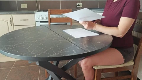 A girl at the kitchen table cuts white paper with scissors Stock Footage 316789946