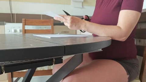 A girl at the kitchen table cuts white paper with scissors Stock Footage 316789948