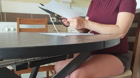 A girl at the kitchen table cuts white paper with scissors Stock Footage 316790121