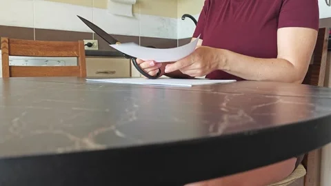 A girl at the kitchen table cuts white paper with scissors Stock Footage 316790316