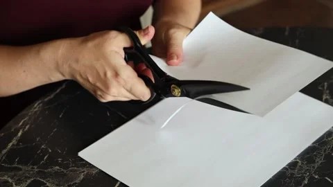A girl at the kitchen table cuts white paper with scissors Stock Footage 316790777