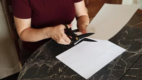 A girl at the kitchen table cuts white paper with scissors Stock Footage 316790936