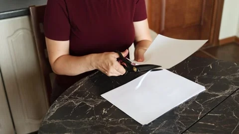 A girl at the kitchen table cuts white paper with scissors Stock Footage 316791058